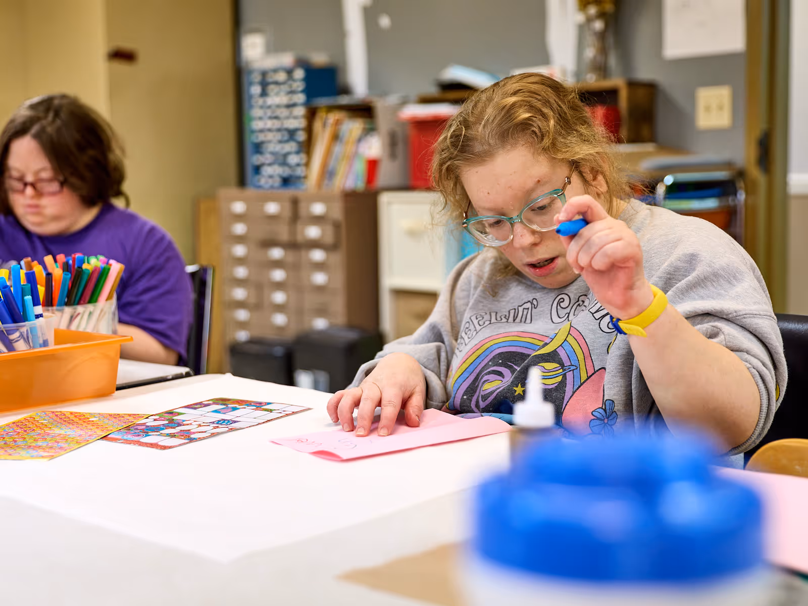 Woman with developmental disabilities seated at a desk drawing with markers, highlighting GentleBrook’s supportive residential services that encourage creativity and independence
